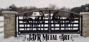 Horse farm driveway gates with silhouettes of four horses at a wooden fence.