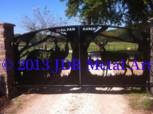 Best driveway gates in the United States, with bear and deer design, each flanking a large tree in the center with mountains in the background.