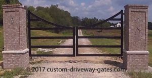 Swinging driveway gates hanging from columns with black powder coat and hinges.