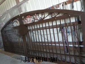 Traditional gates with plasma cut scrolls on top and a plaque in the center. There are pickets and a brown powder coated finish.