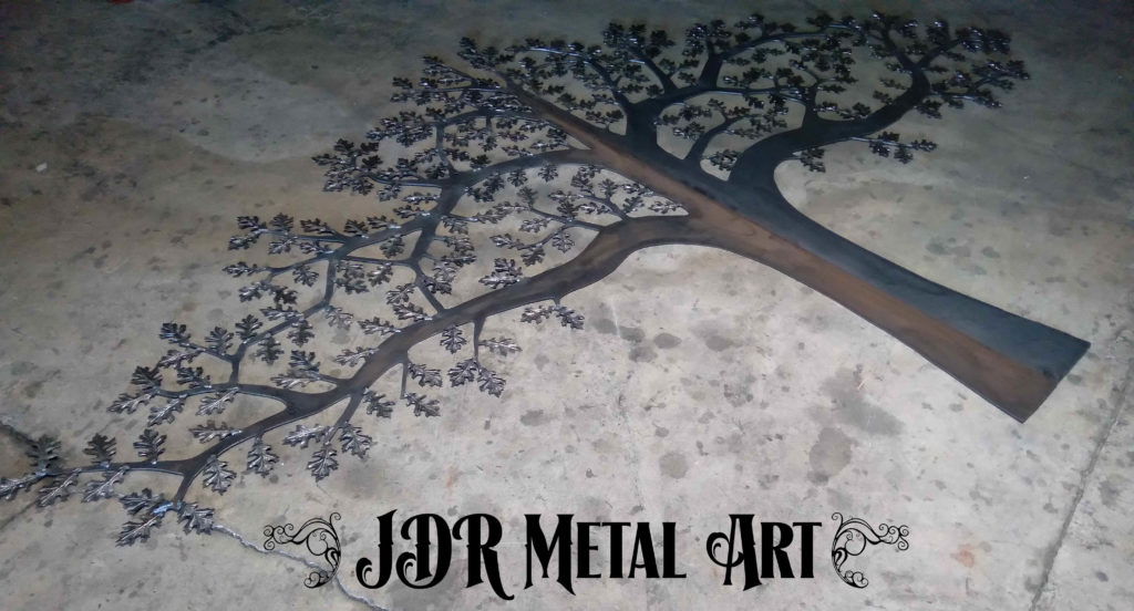 Plasma cut metal tree with oak leaves on concrete floor.