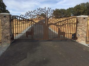 Rustic driveway gates with tree and horse theme on a picket gate frame.