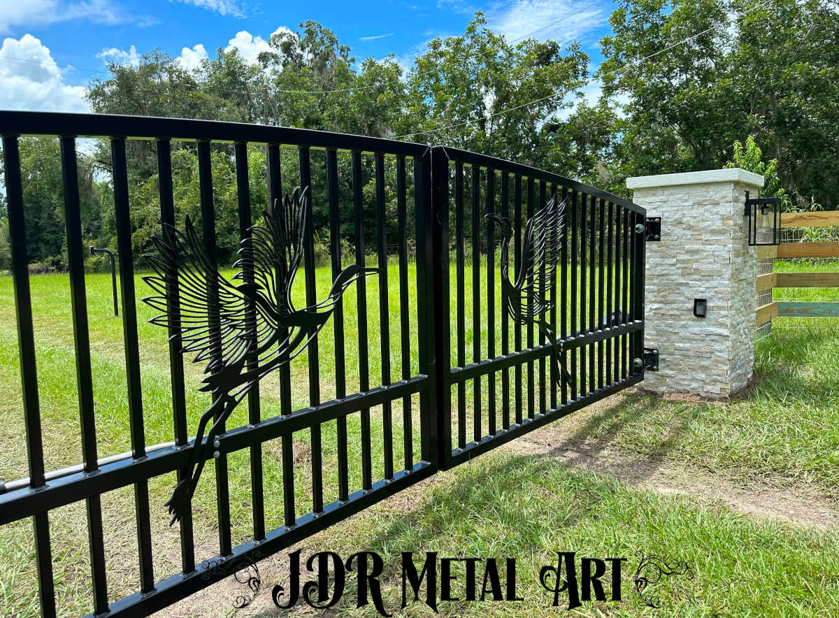 Driveway gate in Gainesville Florida that is arched, black, with custom design, hanging from stone columns.