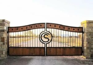 Wood and metal driveway gate design ideas with logo and stars, dual swing hanging from stone columns.
