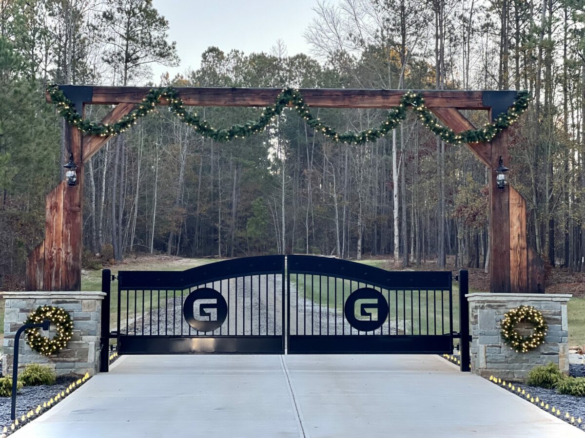 Atlanta driveway gates with wrought iron and black powder coated finish with wood arch overhead and stone columns, and also concrete driveway and gate openers.