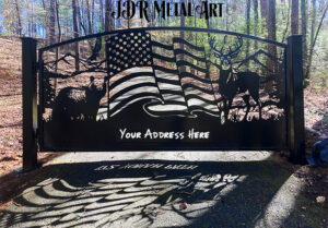 A driveway gate Atlanta made from steel with an arched top and two 6x6 gate posts. The gate design idea includes wildlife such as whitetail deer, a black bear, a bald eagle, a flag and the North Georgia mountains in the background of the scene.