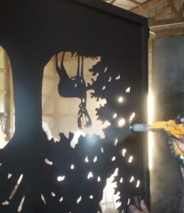 worker powder coating a custom driveway gate using a spray gun