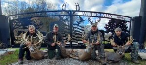 This driveway gate features wildlife, wild animals including deer, turkey, ducks, trees, and American flag, four hunters, with an arched driveway gate hanging from large columns about 20' wide.