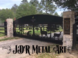 Aluminum driveway gates with metal art wild animals plasma cut a welded into custom gates for driveway that is 20' wide with a cantilever tail section because it is an automated slide gate hung on an aluminum track. Also there are stone columns and an inscription, with the logo of the Honey Lakes Preserve property engraved in the aluminum sheet near the top of the arched gate frame. There are swamp trees and deer, turkeys and turkey hens with pine trees.